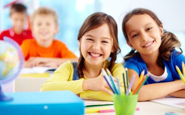 Portrait of two diligent girls looking at camera at workplace with schoolboys on background