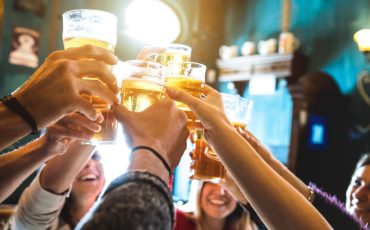 Group of happy friends drinking and toasting beer at brewery bar restaurant - Friendship concept with young people having fun together at cool vintage pub - Focus on middle pint glass - High iso image