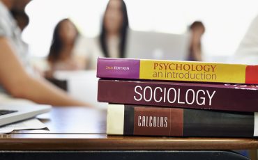 Cropped shot of university text books on a desk with students blurred in the background